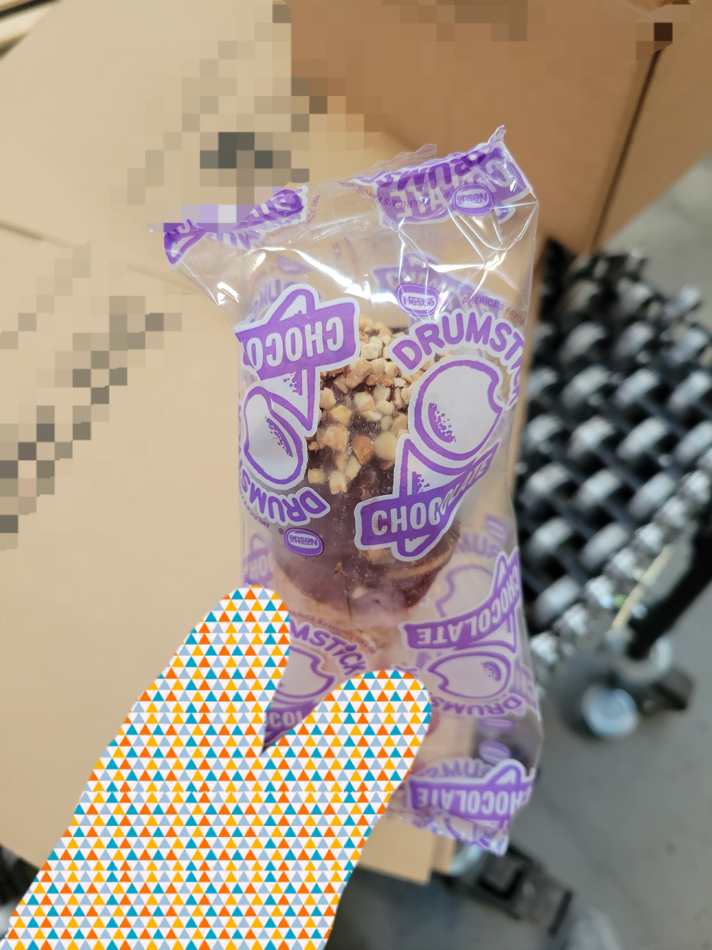 Chocolate drumstick ice cream in plastic held by a hand.